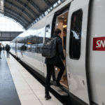 Personne de dos montant dans un train SNCF blanc sur un quai de gare.